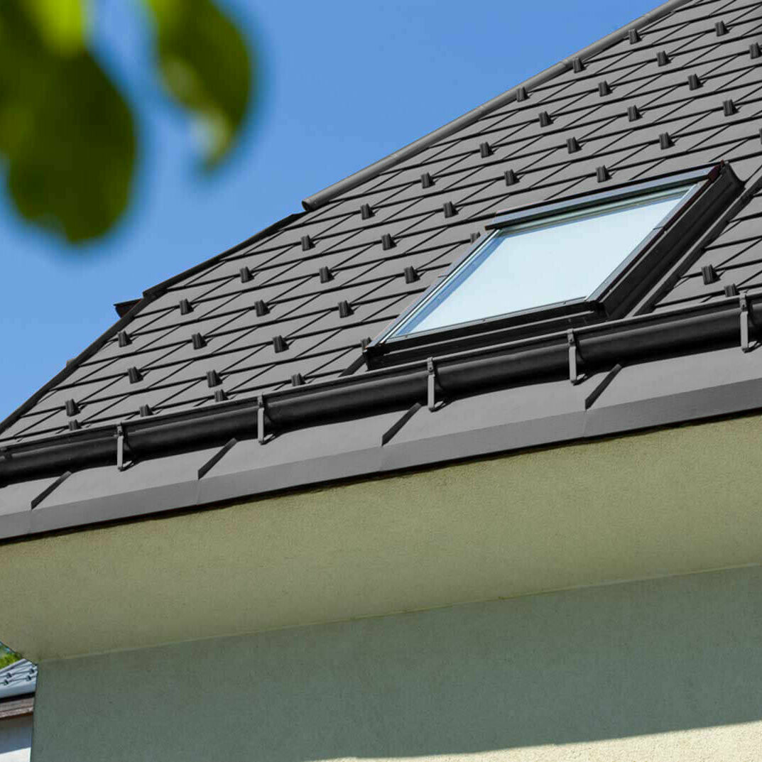 Zdjęcie referencyjne rynny leżącej PREFA z oknem dachowym i czarnym dachem.