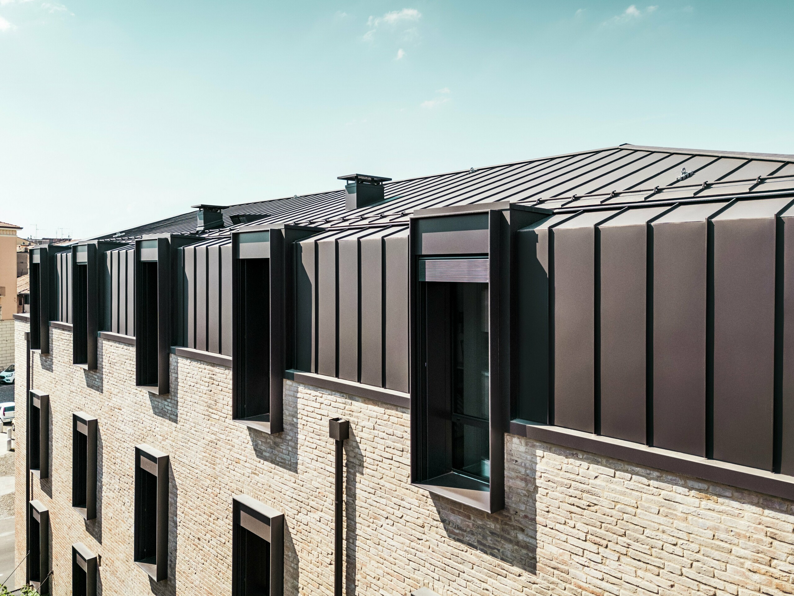 Nowoczesny projekt dachu i fasady domu z cegły we Włoszech z dachem aluminiowym PREFALZ w kolorze P.10 orzechowym i charakterystycznymi świetlikami (szczytami).