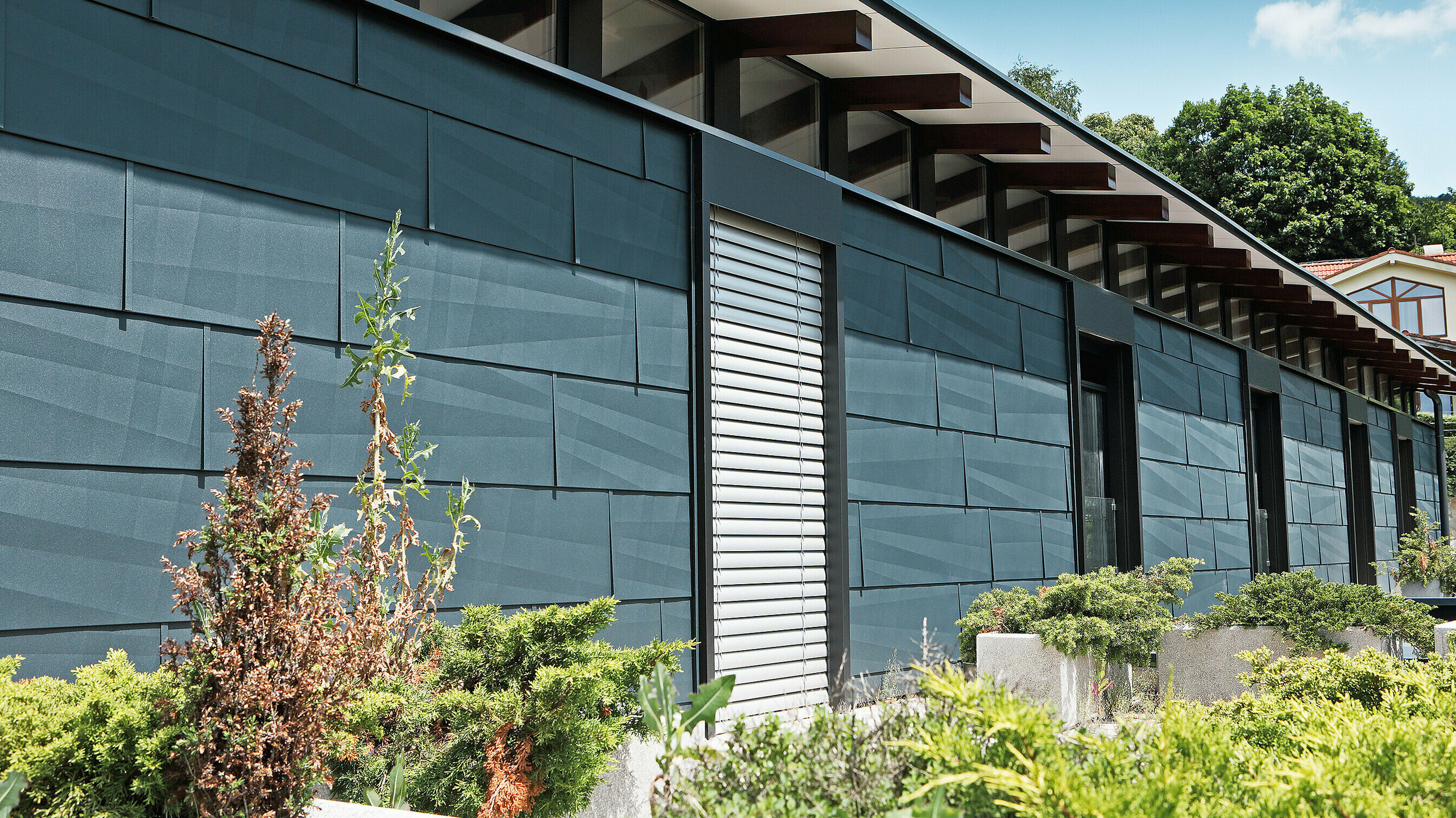 Nowoczesna strona nawietrzna na tle ogrodu zaprojektowana z panelem elewacyjnym FX.12 w kolorze antracytowym.