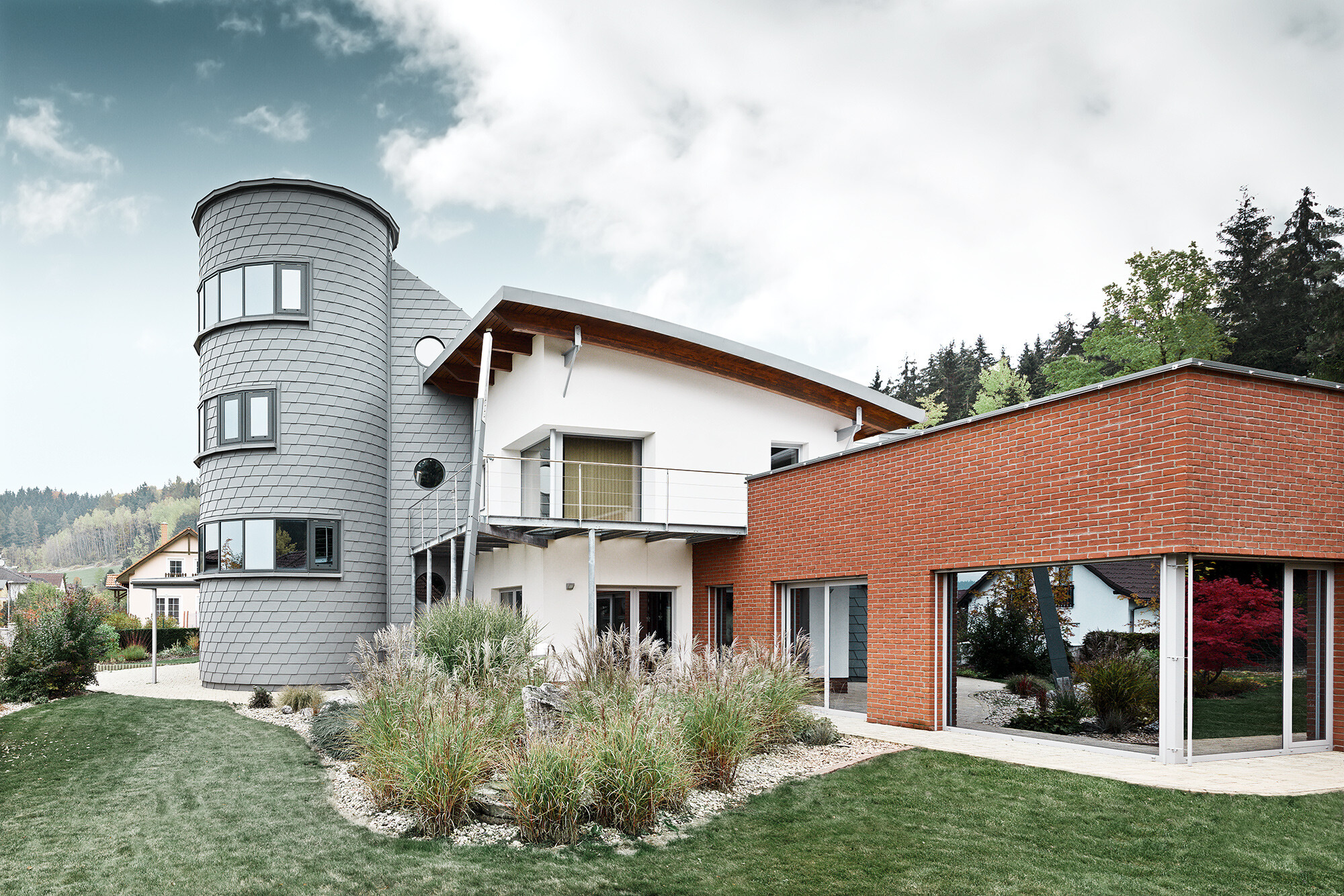 Dom jednorodzinny z przybudówką wieżową, okrągła wieża pokryta jest łupkiem elewacyjnym PREFA w kolorze szarej patyny 