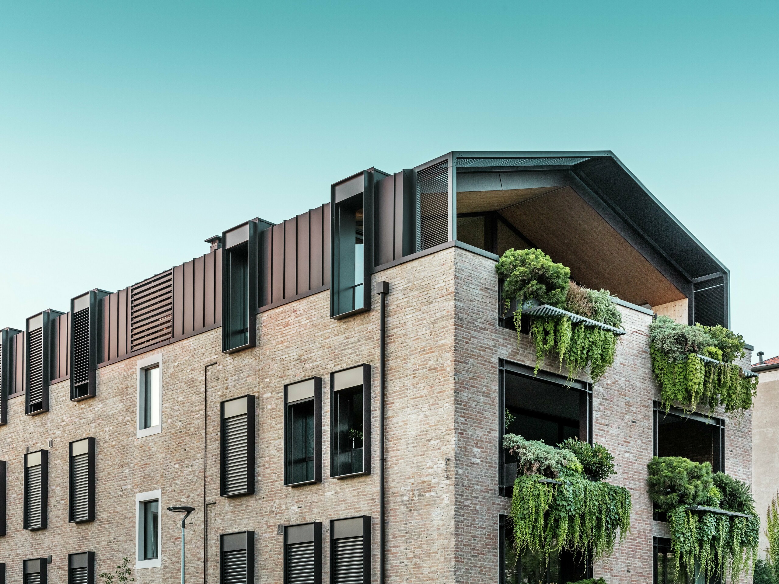Zrównoważony budynek mieszkalny we Włoszech z dachem aluminiowym PREFALZ w kolorze P.10 orzechowym i wiszącymi ogrodami na południowej fasadzie – architektura aktywna klimatycznie z cegłami i terenami zielonymi.