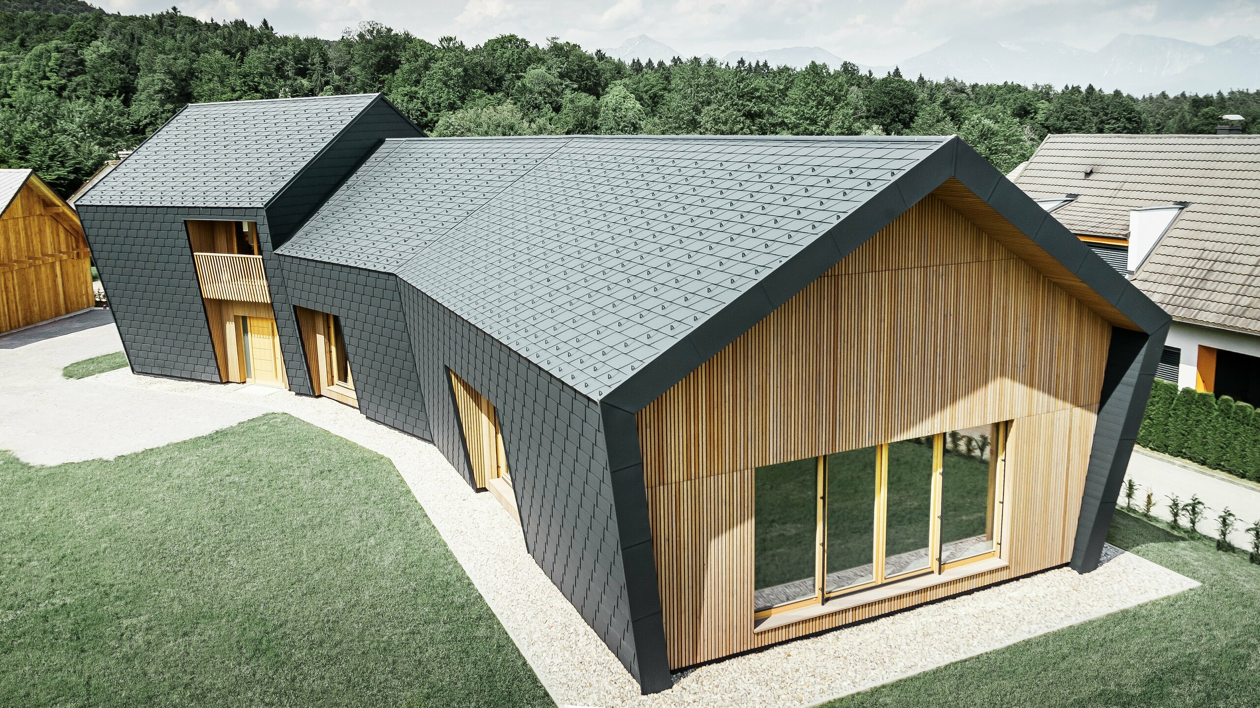 Duże powierzchnie dachu i elewacji pokryte dachówką łupkową DS.19 w kolorze antracytowym P.10, od frontu elewacja została pokryta drewnem