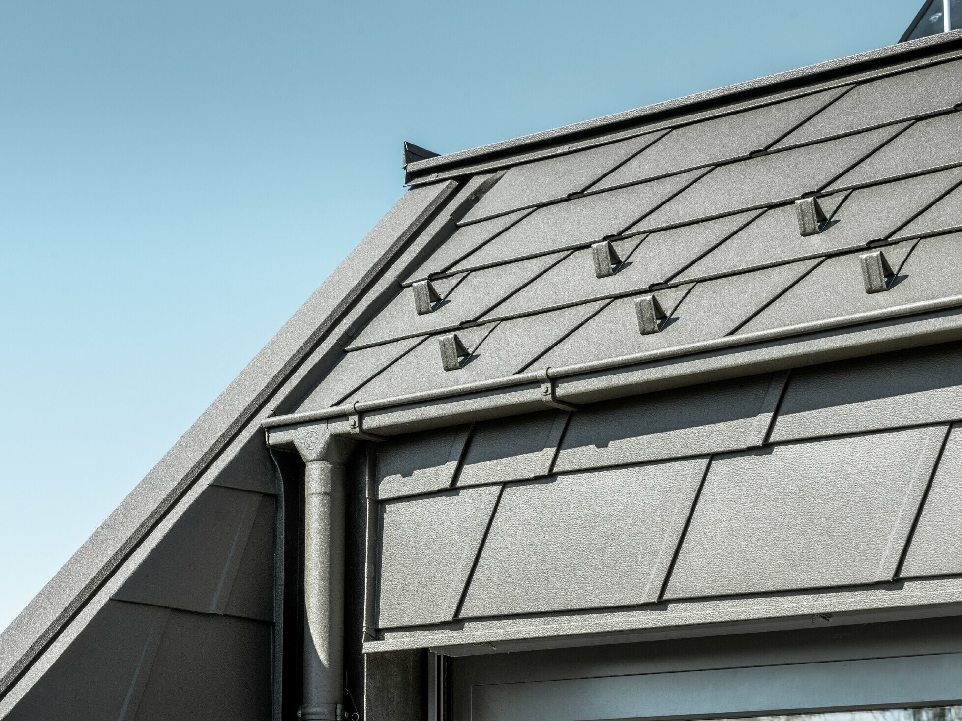 Dachówki aluminiowe PREFA DS.19 ze stoperkami śniegowymi. Odwodnienie dachu zapewnia rura kwadratowa PREFA i rura spustowa w kolorze P.10 brązowym.