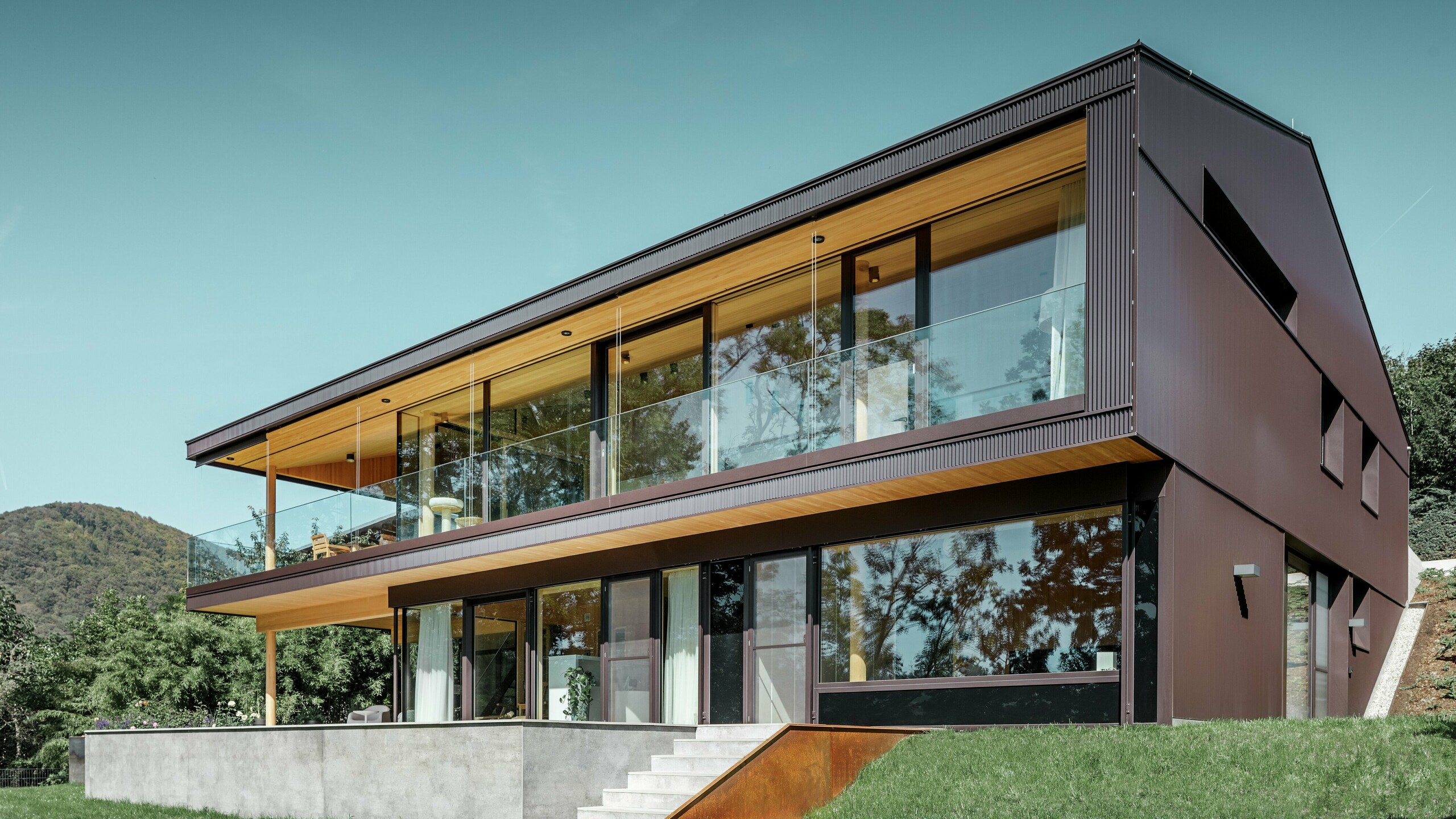 Nowoczesny dom jednorodzinny z dużymi oknami od strony ogrodu i poszyciem elewacji z ciemnobrązowych profili trójkątnych PREFA.