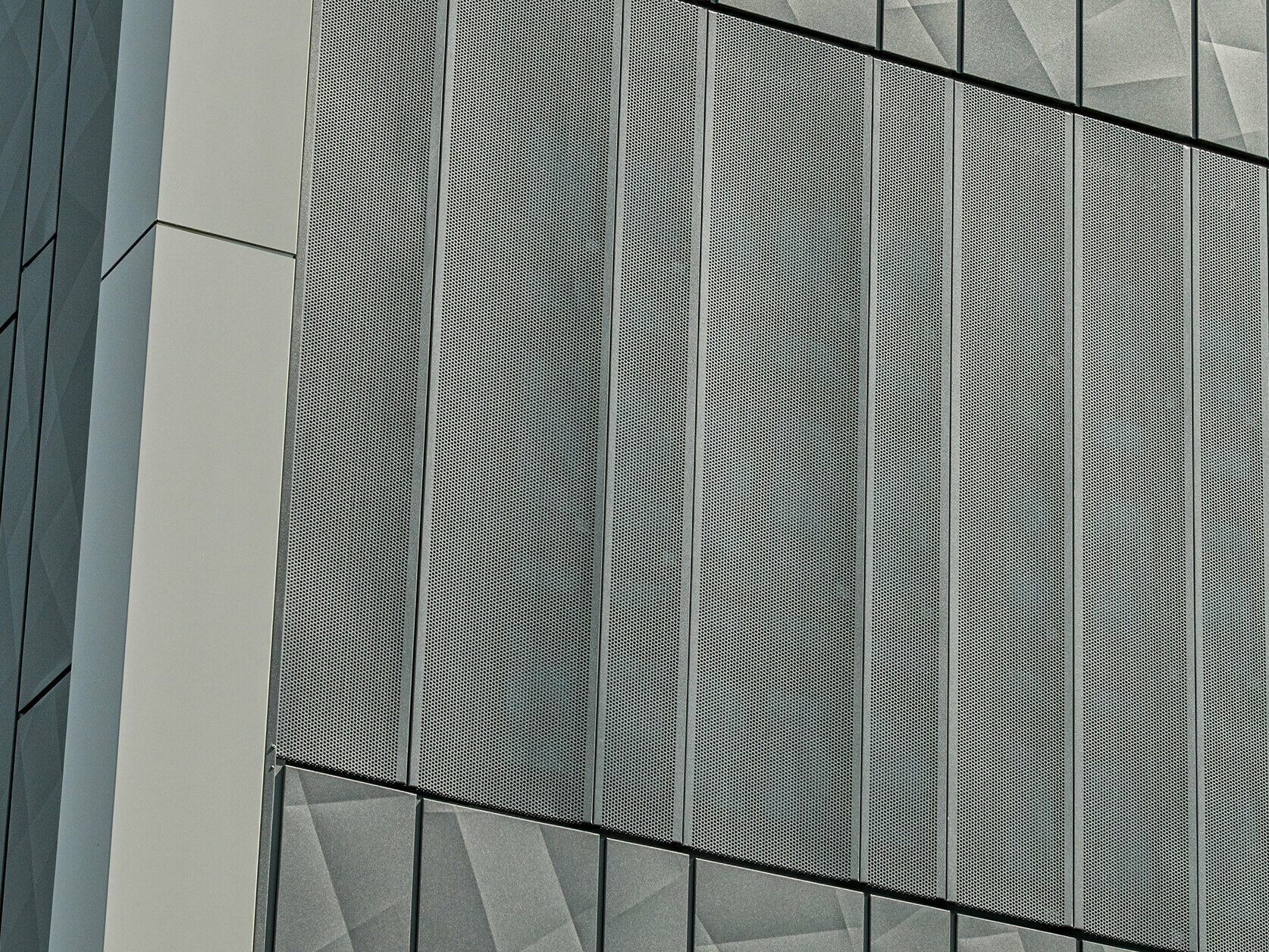 Widok elewacji sklepu Eurospar w Rohrbach z okładziną PREFA Siding.X i perforowanymi okładzinami w kolorze antracytowym. Elementy Siding.X tworzą żywy, geometryczny wzór fug, natomiast perforowane okładziny zapewniają nowoczesną, przepuszczającą powietrze strukturę.