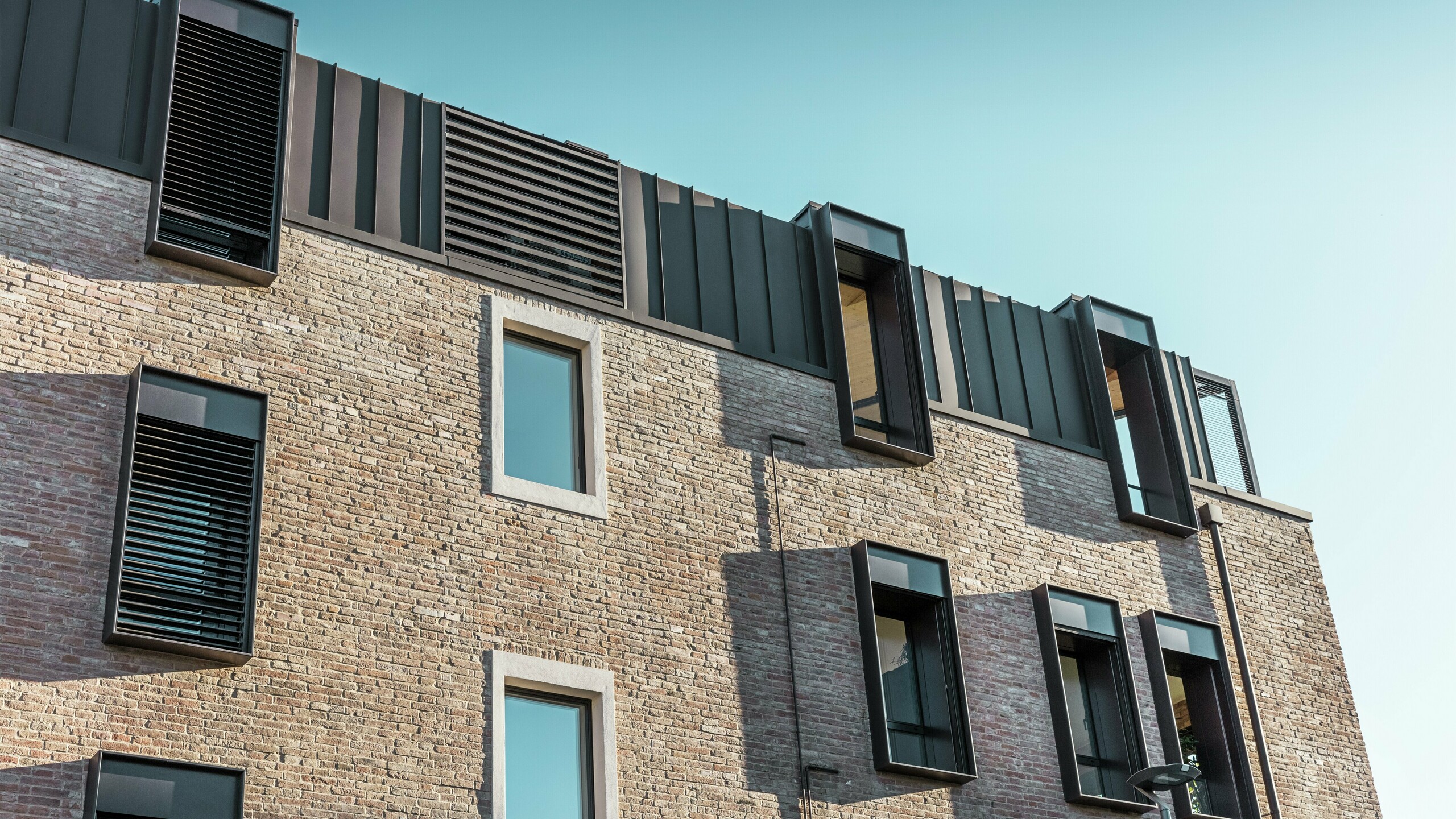 Szczegółowy widok odnowionego domu z cegły we Włoszech z dachem aluminiowym PREFALZ w kolorze P.10 orzechowy brąz i nowoczesnymi lukarnami – udane połączenie tradycyjnej konstrukcji ceglanej i współczesnej architektury.