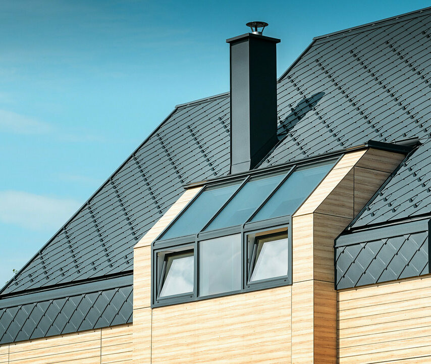 Dom jednorodzinny z dachem dwuspadowym bez występu dachowego, z elewacją o wyglądzie drewna i dachem aluminiowym w kolorze antracytowym
