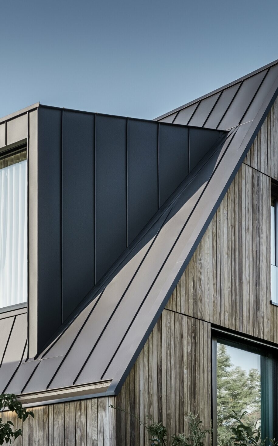 Stromy dach dwuspadowy z dużą lukarną, pokryty PREFALZ w technologii rąbka stojącego od PREFA w kolorze antracytowym, w połączeniu z elewacją